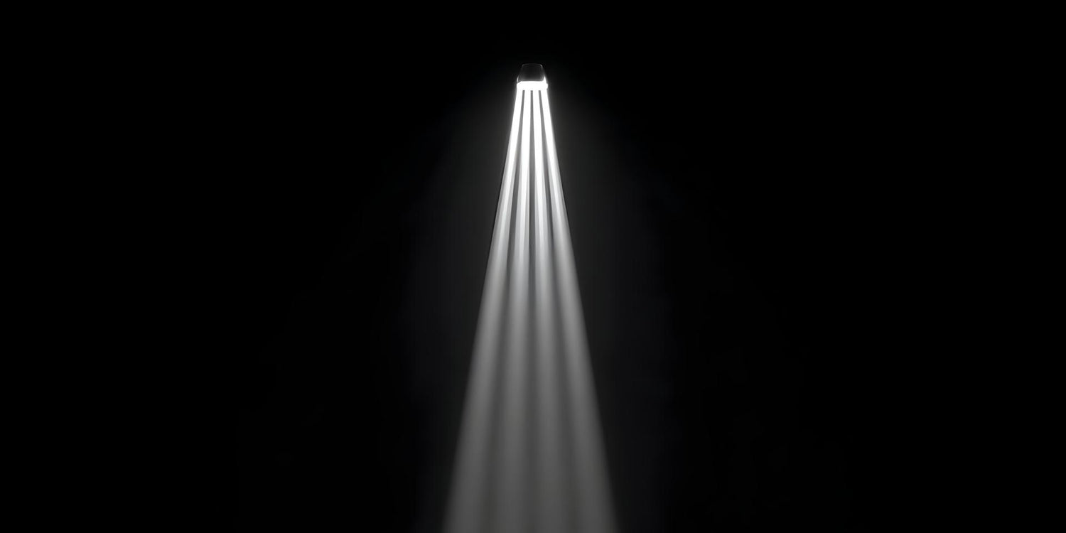 A single bright spotlight shines multiple white light rays downwards on a black background