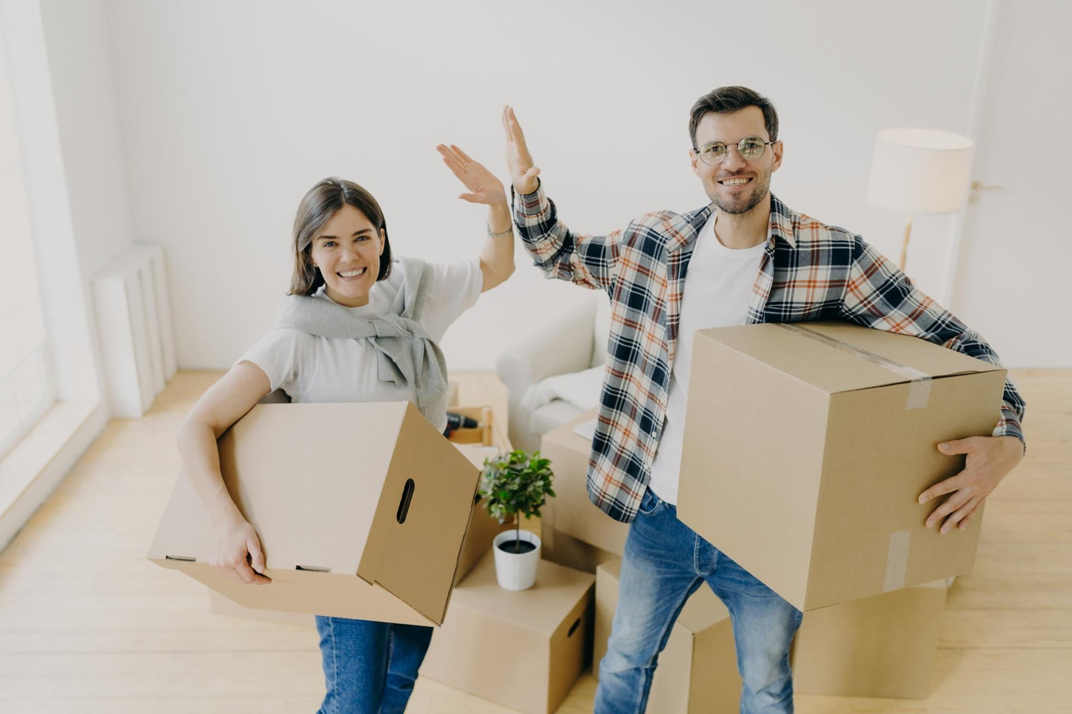 Photo of cheerful young woman and man give high five, smile pleasantly at camera, dressed in casual clothes, start new life, stand in spacious light bedroom. People, repairing and moving concept